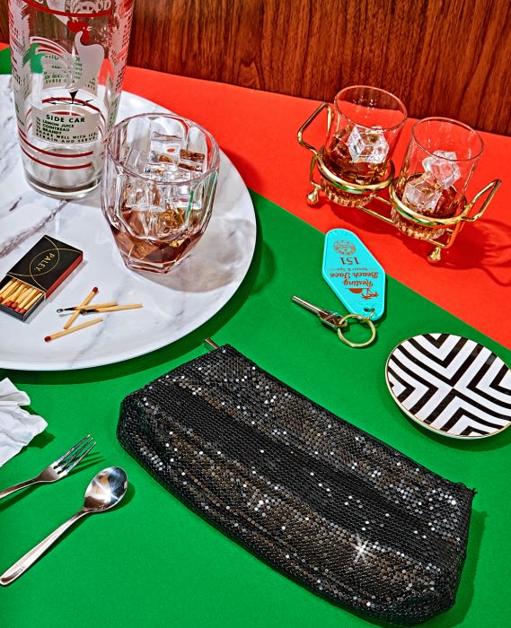 Still life shot with cocktail glasses, a black clutch, and other retro accessories against a vibrant green and red backdrop.