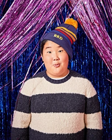 Portrait of an Asian adult in a striped sweater and beanie with the text RAD against a blue and purple metallic fringe backdrop.