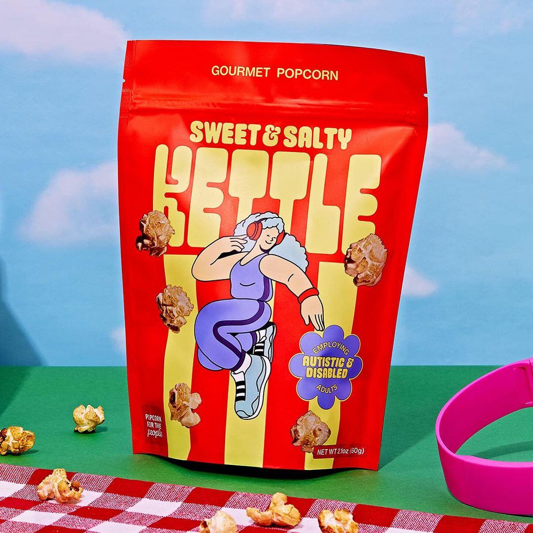 Bright image of a red bag of Sweet & Salty Kettle gourmet popcorn with a whimsical design, set on a checkered tablecloth.