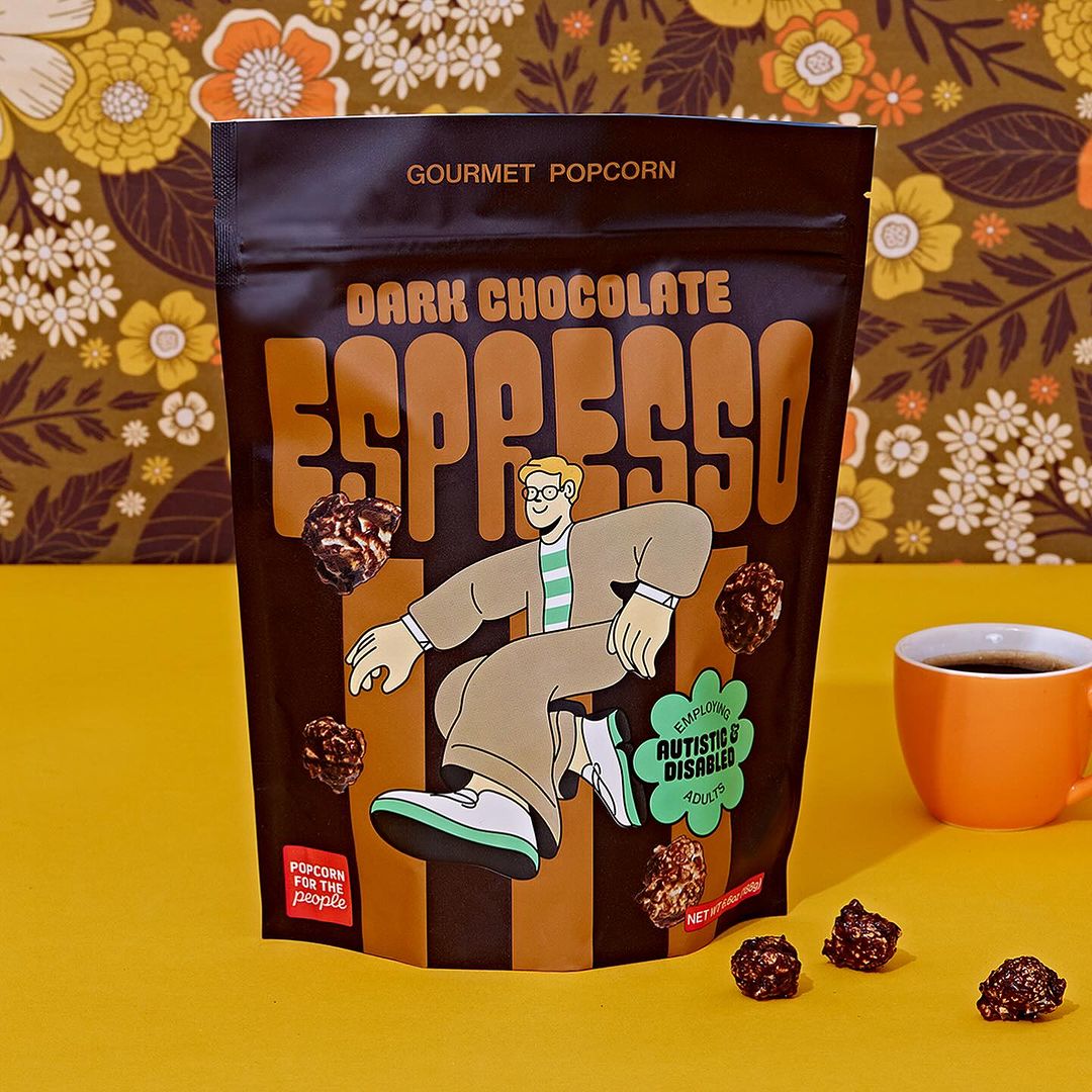Eye-level studio shot: package of Dark Chocolate Espresso popcorn with cartoon figure, floral backdrop, and cup of black coffee.