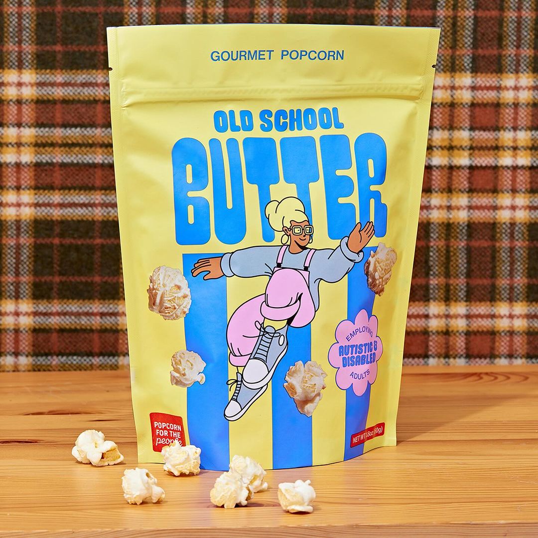 Bag of gourmet popcorn with cartoon character and floating popcorn on a wood surface and brown plaid background, studio shot.