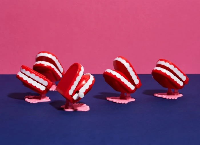 Several wind-up chattering teeth toys stand on a blue surface against a background with a pink top and a blue bottom.