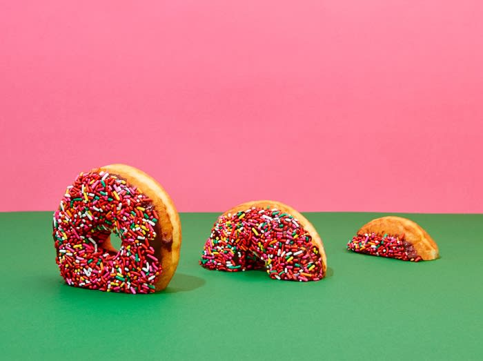 Three donuts decorated with sprinkles are arranged on a green surface against a pink background, creating a visually appealing food still life.
