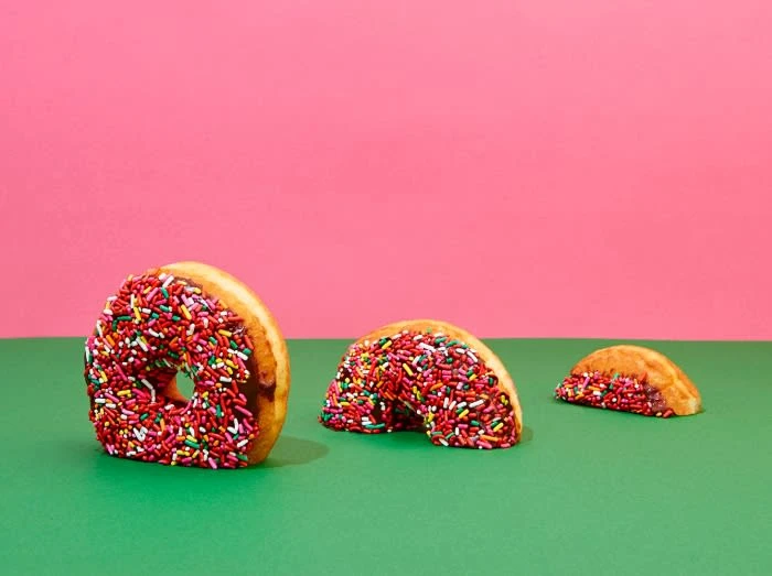 Three donuts decorated with sprinkles are arranged on a green surface against a pink background, creating a visually appealing food still life.