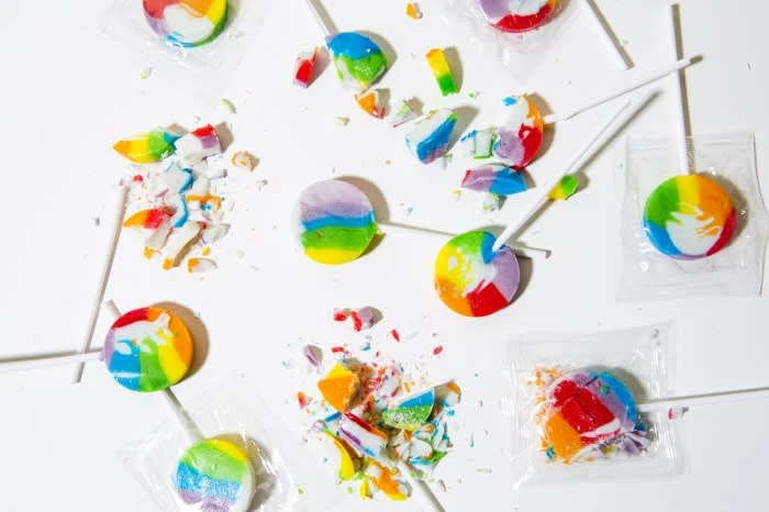 Overhead shot of rainbow swirl lollipops, some broken into pieces, scattered on a white surface in a flat lay composition.