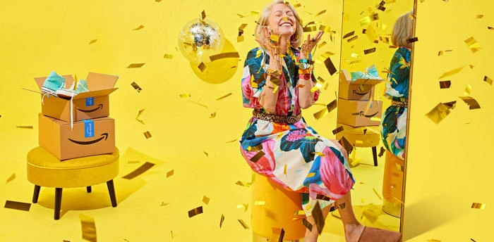 Blonde woman in floral dress celebrates online shopping with confetti, boxes, and a disco ball against a bright yellow background.