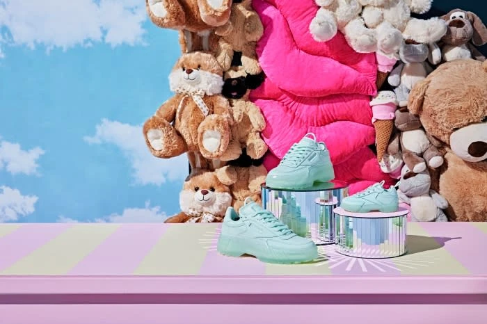 Two pairs of light blue sneakers on a striped surface with various stuffed animals in the background against a sky backdrop.