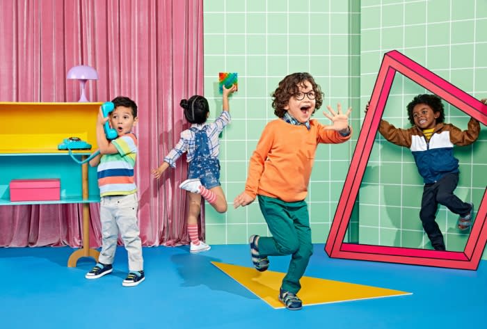 Four kids in a colorful studio, one holding a phone, one with a frame, one with a building block, and one in overalls. 