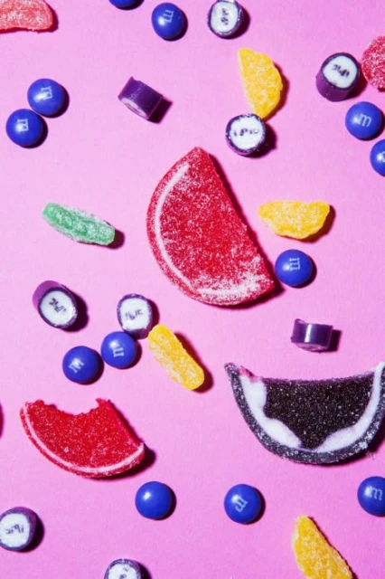 Overhead shot of scattered fruit-flavored gummy candy and blue M&Ms on a pink background creates a bright, playful, colorful food composition.