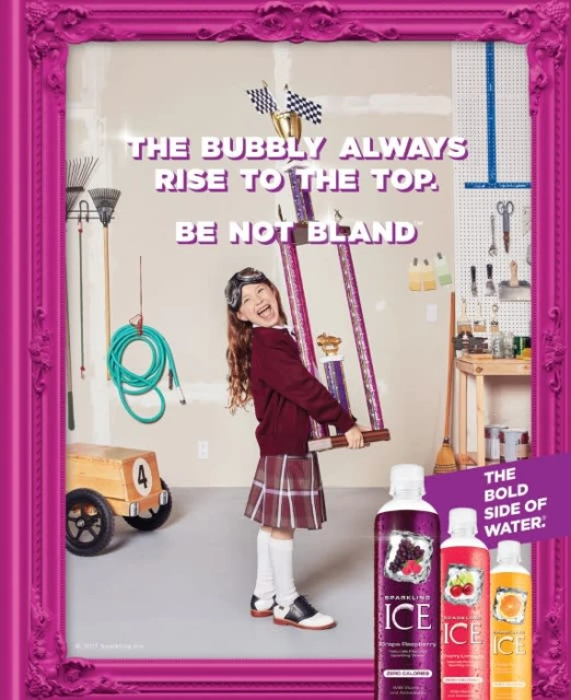 Smiling child holding trophy with Sparkling Ice drinks in a magenta frame in a garage setting, displaying playful beverage advertising.