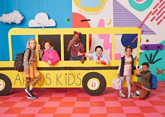 A group of six kids posing in front of a large cardboard school bus cutout, set against a vibrant and playful backdrop.
