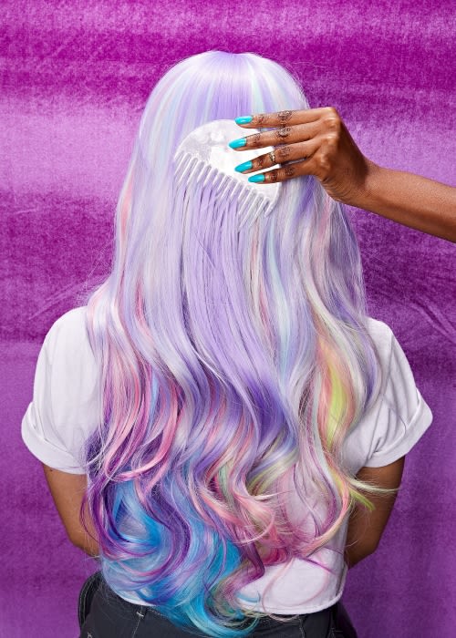 Person combing long, wavy pastel rainbow hair. Close-up studio shot against a textured purple background. Hair salon and beauty concept.