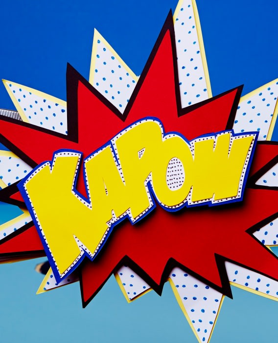 Red, yellow, and white paper art in a comic book style with text 'KAPOW' on a blue background for party decoration or visual communication.