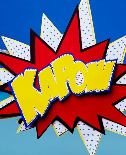 Red, yellow, and white paper art in a comic book style with text 'KAPOW' on a blue background for party decoration or visual communication.