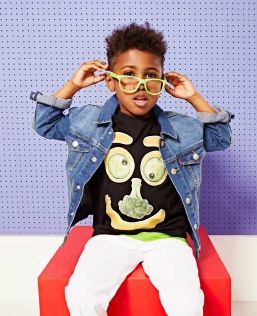 Child in playful portrait, wearing glasses and food-themed t-shirt, seated against a dotted background. Bright, youthful style.