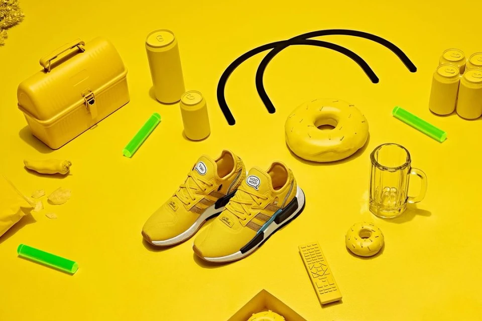 Overhead shot of yellow Adidas sneakers, yellow lunchbox, donuts, and cans on a yellow surface, creating a vibrant, monochromatic still life.