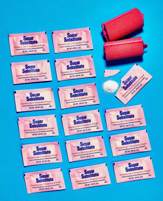 Arrangement of sugar substitute packets and pink hair rollers on a bright blue background, creating a vibrant and contrasting aesthetic.