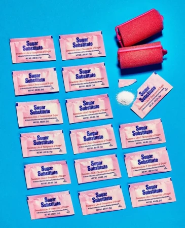 Arrangement of sugar substitute packets and pink hair rollers on a bright blue background, creating a vibrant and contrasting aesthetic.