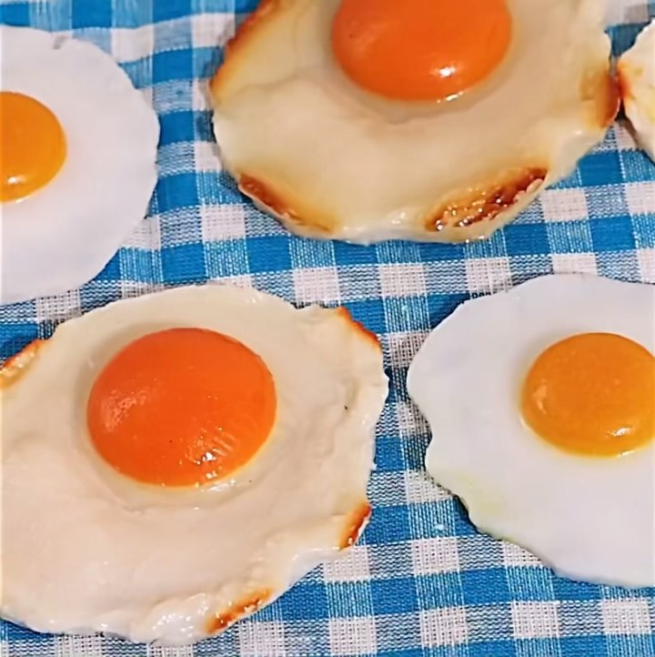 Several fried eggs with bright orange yolks on a blue and white checkered tablecloth, creating a vibrant and appetizing food still life.