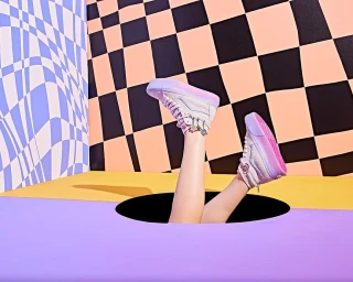 Legs in high-top sneakers emerging from a hole in a brightly colored set with checkered and wavy patterns.