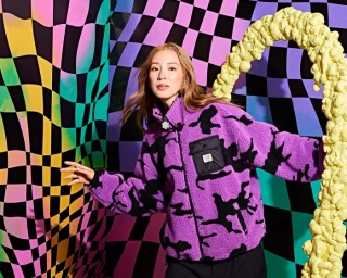 Woman in purple fleece jacket posing against a vibrant checkered backdrop photographed by Meiko Arquillos