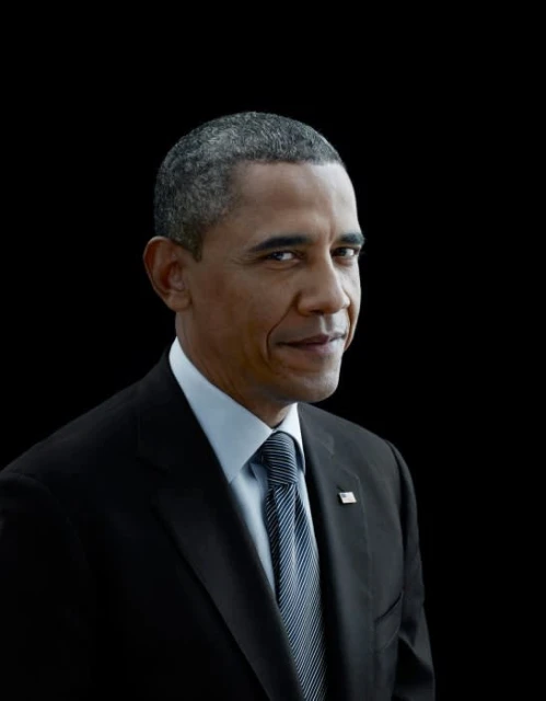 Portrait of Barack Obama in a dark suit with an American flag lapel pin against a solid black background.