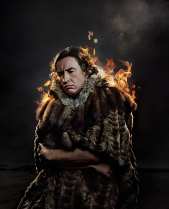 Adult male wrapped in a fur cloak, illuminated by side studio lighting and set against a dark background with visual effects of fire.