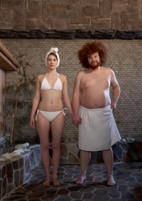 A couple stands side-by-side in a sauna. The woman wears a white bikini and the man wears a white towel wrapped around his waist.