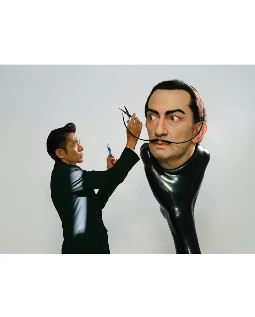 Asian adult male cuts the mustache of a mannequin of a male's head with scissors in a photo studio with a white background.