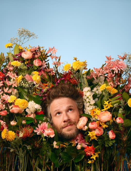 Man's head and shoulders surrounded by vibrant flowers against a blue sky backdrop, creating a whimsical, nature-infused portrait.