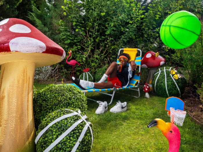 A person in sunglasses lounges in a beach chair on grass surrounded by decorative mushrooms and a basketball with playful outdoor vibes.