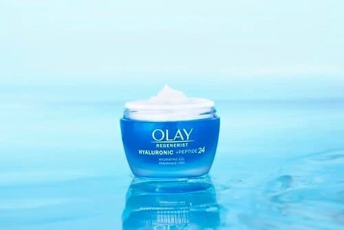 Olay Regenerist Hyaluronic and Peptide 24 hydrating gel fragrance-free jar in blue packaging, cream visible on top, water background.