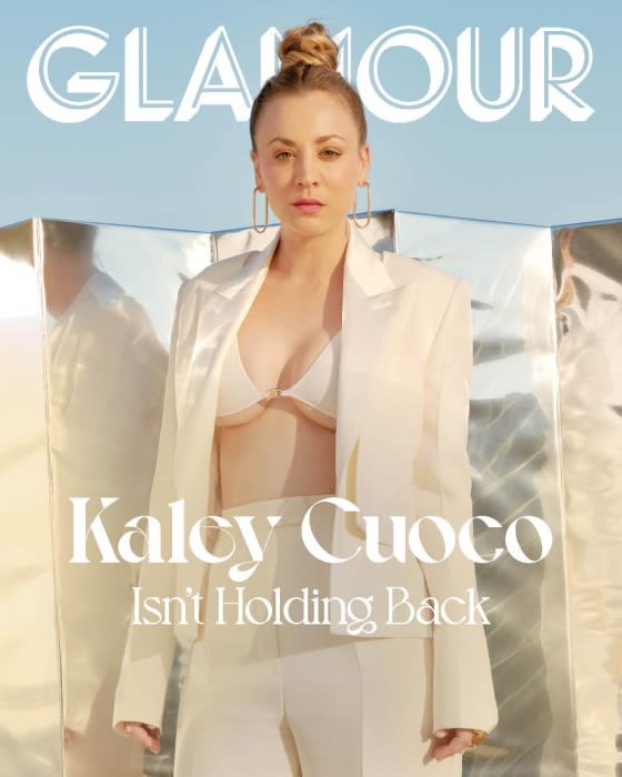 Glamour magazine cover featuring Kaley Cuoco in a white suit, standing outdoors against a metallic backdrop and a light blue sky.