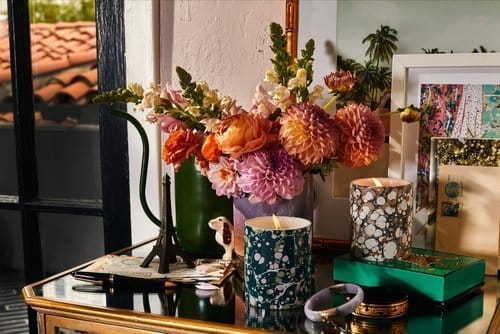 Indoor still life of orange and pink flowers in vases on a table, with lit candles and a model of the Eiffel Tower.