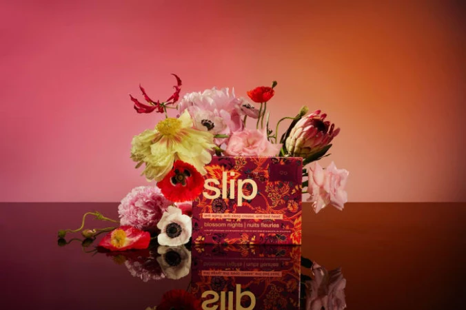 Slip Blossom Nights product box surrounded by colorful flowers on a reflective surface and warm gradient background.
