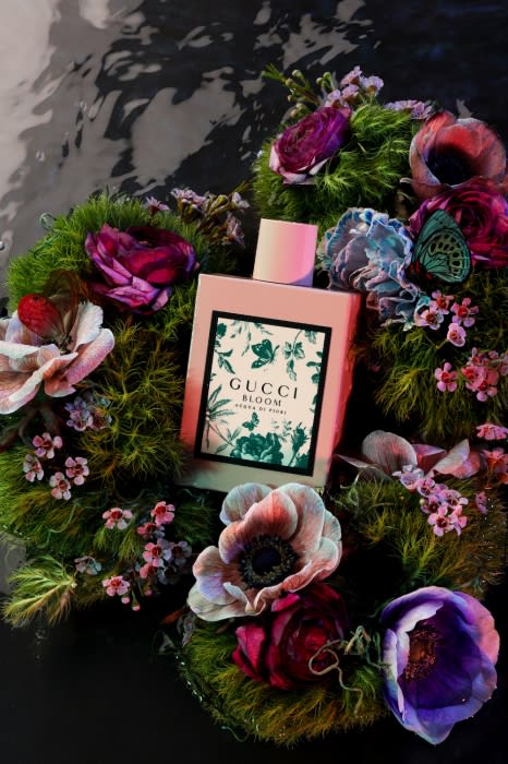 Gucci Bloom perfume bottle surrounded by colorful flowers and greenery with a dark background, beauty and fragrance concept.