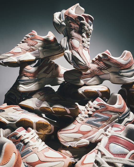 Pile of New Balance 9060 sneakers in white and peach tones, stacked in a studio with soft lighting and a gray gradient backdrop.