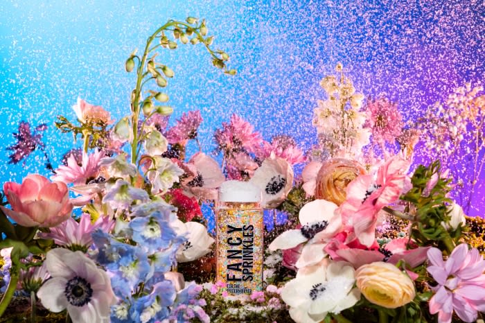 Sprinkles container surrounded by colorful flowers against a blue and purple backdrop, creating a vibrant and whimsical composition.