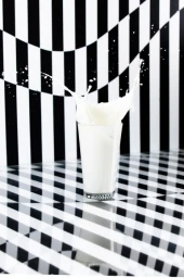 Glass of milk with a dramatic white splash against a warped black and white striped background