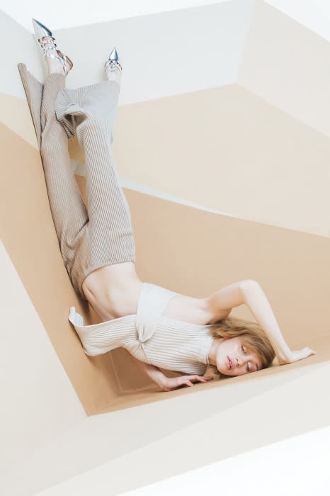 Fashion editorial shot featuring a model in a cream-colored outfit and silver shoes, posing in a geometric, angular setting.