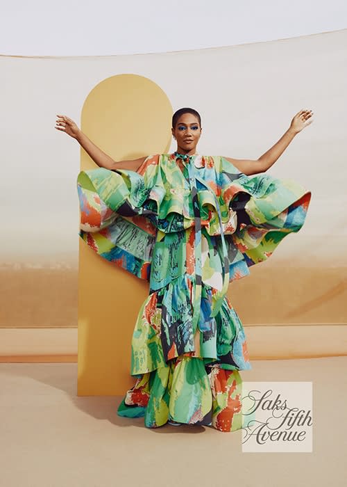 Woman poses in a tiered, vibrant dress with brushstroke patterns against a studio backdrop, showcasing fashion and style.