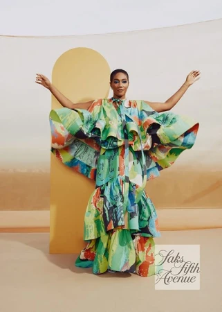 Woman poses in a tiered, vibrant dress with brushstroke patterns against a studio backdrop, showcasing fashion and style.