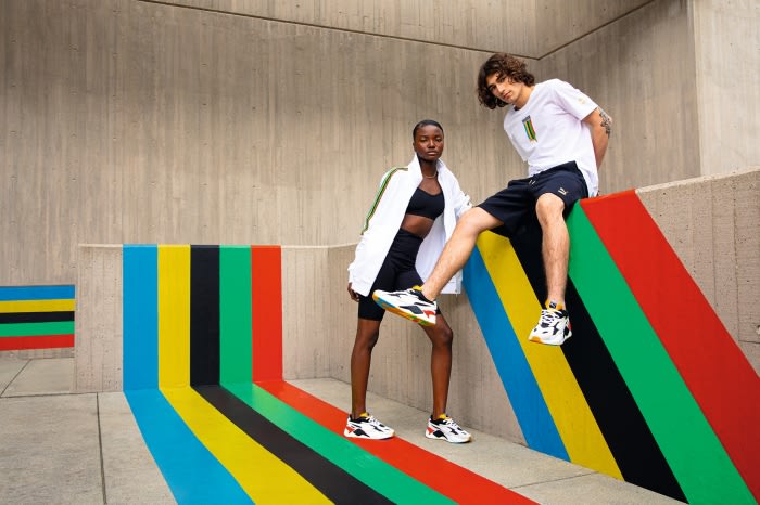Two fashion models pose in PUMA athletic wear, including sneakers, against a colorful striped wall and concrete architectural background.