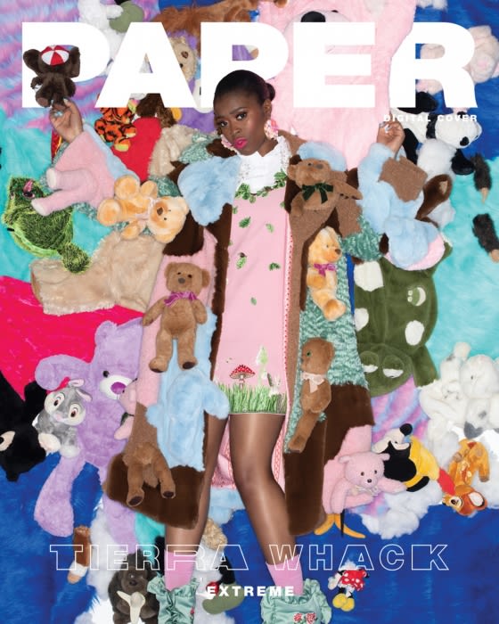 A young woman with dark hair stands on a colorful background surrounded by plush toys in a magazine cover-style fashion photograph.
