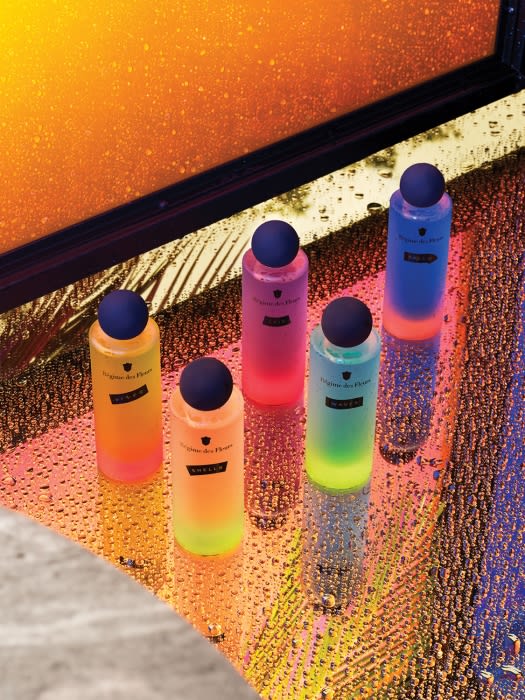 Five colorful perfume bottles with sphere-shaped caps, displayed on a reflective, wet surface with an out-of-focus background.