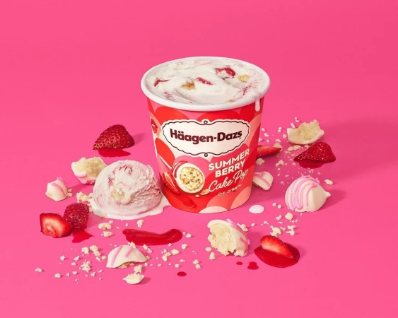 Haagen-Dazs Summer Berry Cake Pop ice cream tub and scoop with strawberries and bite-sized cake pieces scattered around on pink surface.