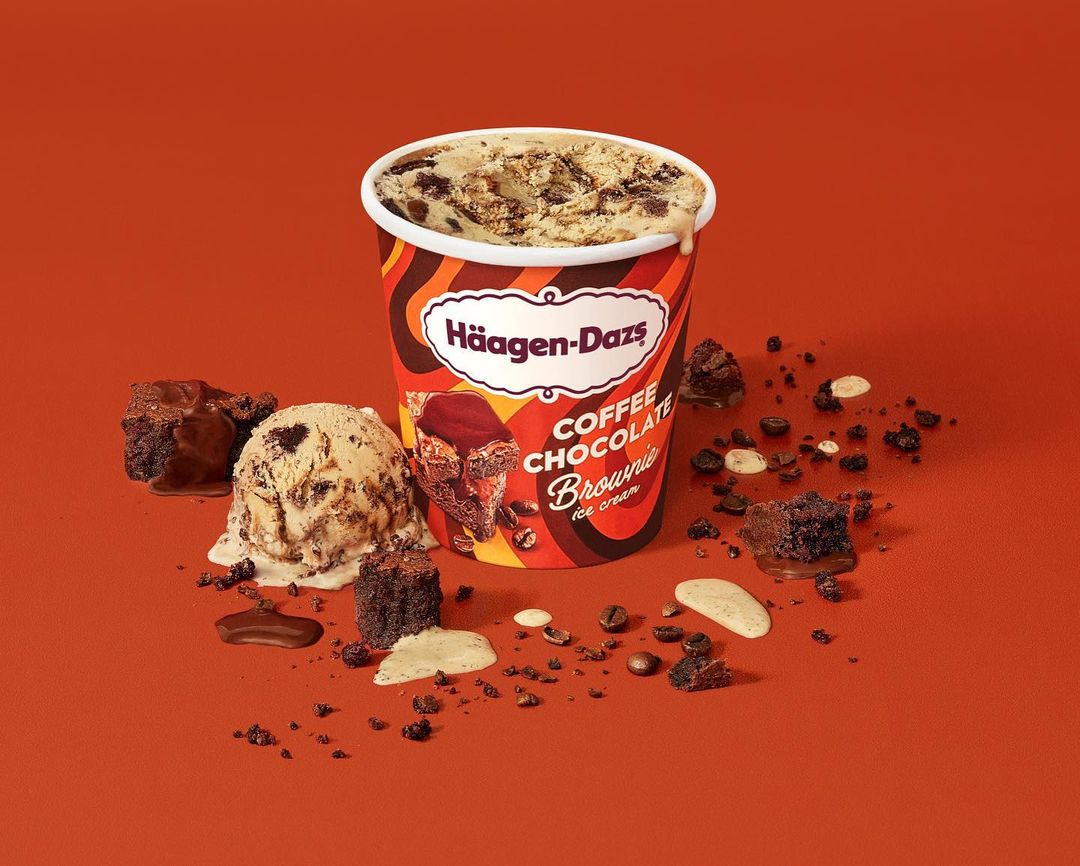 Coffee Chocolate Brownie ice cream pint by Häagen-Dazs with brownie pieces and coffee beans, set against an orange background.