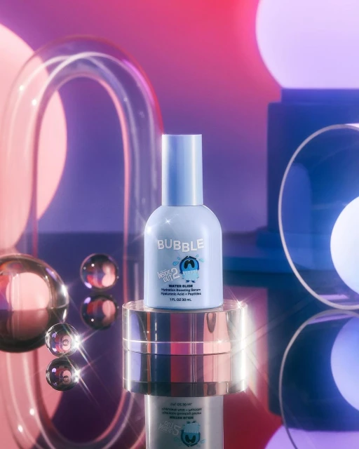 Light blue Bubble skincare bottle with serum on a gold pedestal, surrounded by glass orbs and tubes against a gradient purple background.