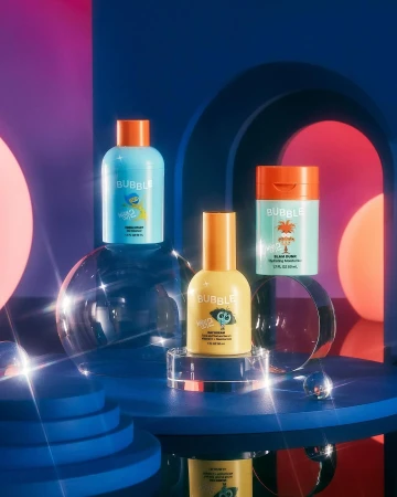 Three Bubble skincare product bottles are displayed on a blue platform with transparent spheres and a vibrant, colorful backdrop.