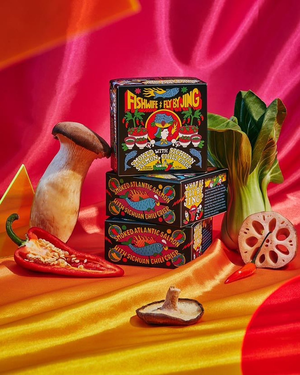 Stacked Fishwife & Fly By Jing canned salmon with bok choy, peppers, mushrooms, and lotus root on orange-and-pink draped fabric.